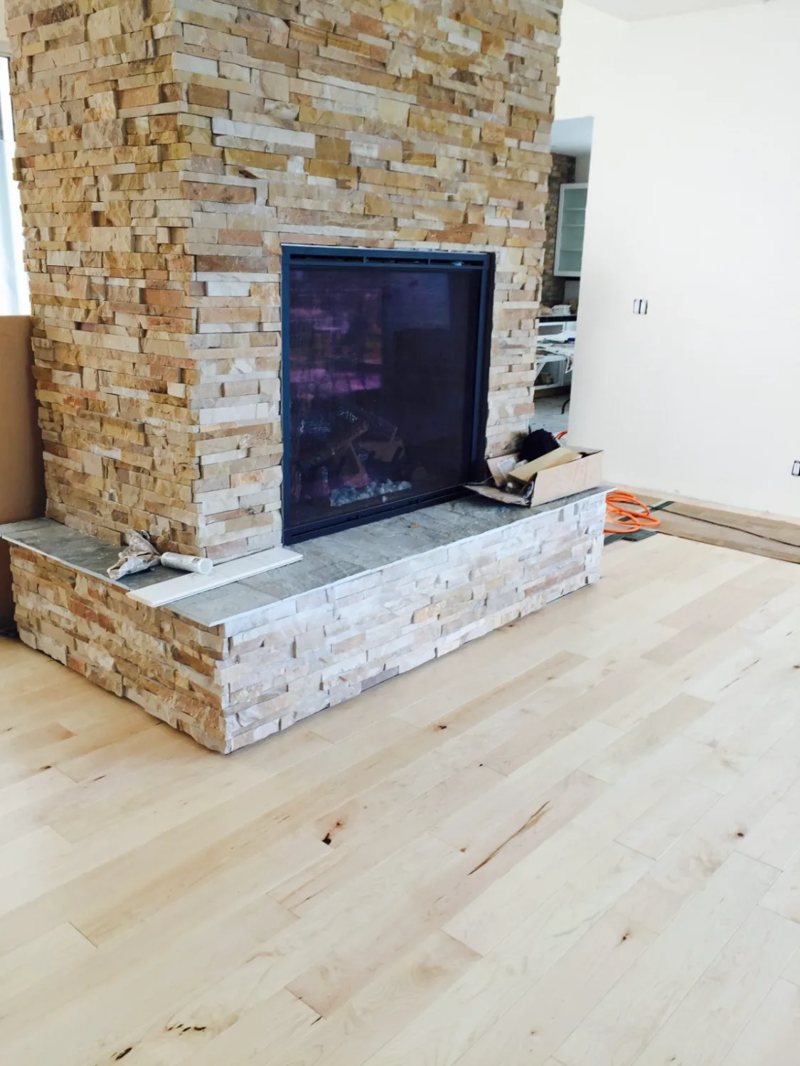 Light maple hardwood flooring beside a stone fireplace